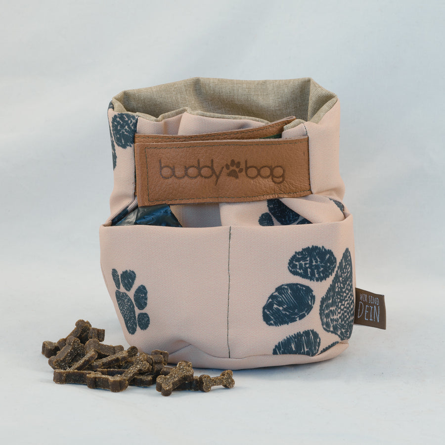 Buddybag in Rosé mit Pfotenmuster, davor Hundeleckerlis